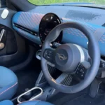 2025 Mini Aceman interieur met blauw gerecycled gebreid stofdashboard, circulair touchscreen-display, stuurwiel met stofband detail, en blauwe bekleding met oranje biezen