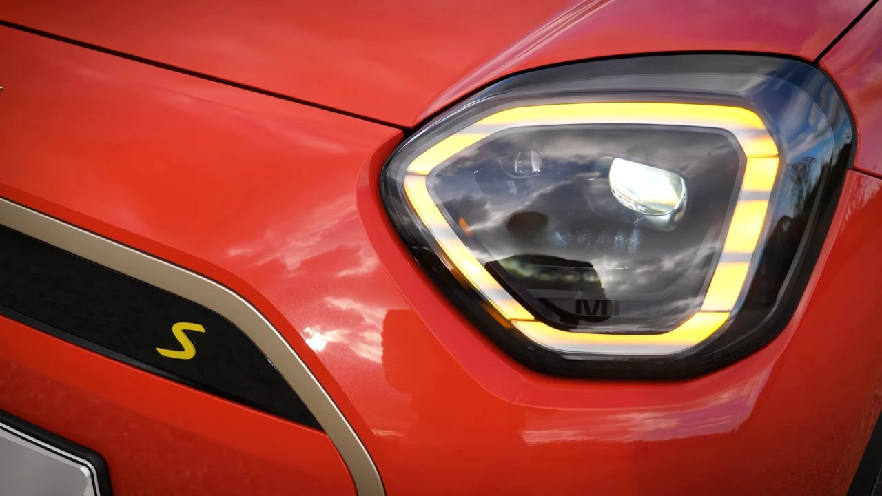 Gedetailleerd zicht van Mini Aceman hoekige LED-koplampbehuizing met verlichte gele DRL-ring, hoofd-LED-projector en gele "S" elektrische aanduiding badge op rode carrosserie