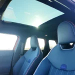Mini Aceman interieur vanuit achter perspectief met groot panoramisch glazen schuifdak, blauwe leren stoelen, en heldere luchtige cabine-atmosfeer