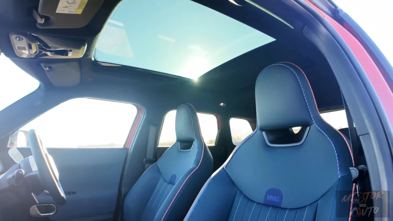 Mini Aceman interieur vanuit achter perspectief met groot panoramisch glazen schuifdak, blauwe leren stoelen, en heldere luchtige cabine-atmosfeer