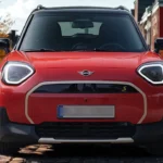 Vooraanzicht van rode Mini Aceman elektrische crossover met gesloten paneel grille, hoekige LED-koplampen met witte DRL, Mini-badge en geel "S" elektrisch symbool op Europese herfststraat