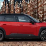 Profielzicht van rode Mini Aceman met crossover carrosseriestijl, vijf deuren, zwart contrastdak, wielkasbescherming en compacte SUV-proporties op bakstenenstraat