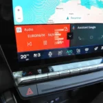 Gedetailleerd beeld van het infotainment van de 2025 Renault Austral toont audio bediening, klimaat instellingen en Google Assistant integratie met fysieke klimaat knoppen eronder.
