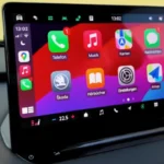 2025 Škoda Enyaq 13-inch touchscreen infotainment systeem met Apple CarPlay interface, diverse app iconen en kleurrijke achtergrond
