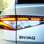 Gedetailleerd beeld van 2025 Škoda Enyaq LED achterlicht met dynamische oranje richtingaanwijzers en ENYAQ letters op witte SUV carrosserie