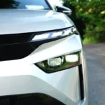 2025 Škoda Enyaq elektrische SUV vooraanzicht in Moon White metallic kleur met LED Matrix koplampen, zwart rooster en ŠKODA badge op kinderkopjes straat met stedelijke gebouwen op de achtergrond