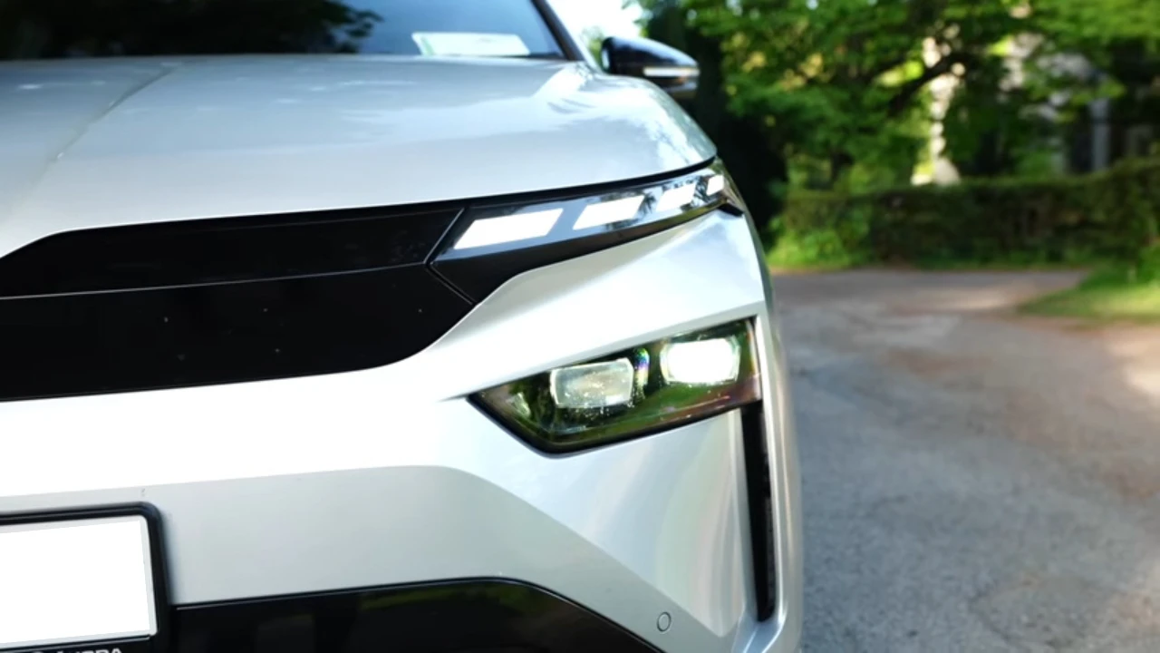 2025 Škoda Enyaq elektrische SUV vooraanzicht in Moon White metallic kleur met LED Matrix koplampen, zwart rooster en ŠKODA badge op kinderkopjes straat met stedelijke gebouwen op de achtergrond