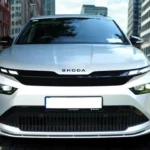 2025 Škoda Enyaq elektrische SUV vooraanzicht in Moon White metallic kleur met LED Matrix koplampen, zwart rooster en ŠKODA badge op kinderkopjes straat met stedelijke gebouwen op de achtergrond