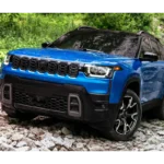 2026 Jeep Cherokee hybride SUV in levendige blauwe kleur gepositioneerd op rotsachtig off-road terrein, vooraanzicht drie-kwart hoek met onderscheidende zeven-slot grille, LED-koplampen en zwarte beschermende bekleding