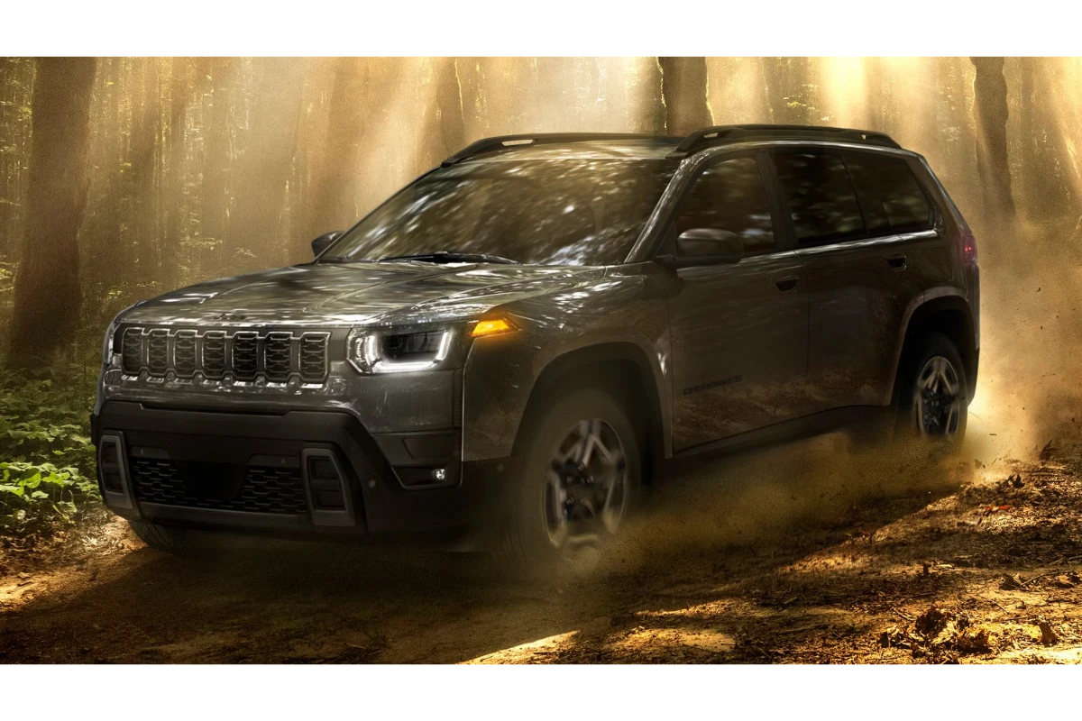 2026 Jeep Cherokee hybride SUV in grijze kleur rijdend door bospad met stofwolken, zijprofiel aanzicht met verhoogde bodemvrijheid en avontuur-klaar ontwerp in natuurlijke verlichting