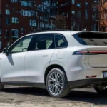 Achter driekwart zicht van 2025 Leapmotor C10 REEV in Pearl White met LED achterlichten, Leapmotor branding, achterruit, dakspoiler en algehele achterontwerp op stadsstraat met appartementengebouwen.