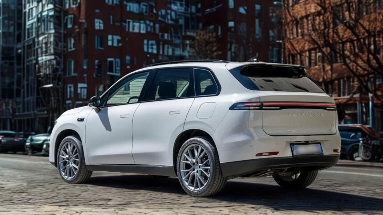 Achter driekwart zicht van 2025 Leapmotor C10 REEV in Pearl White met LED achterlichten, Leapmotor branding, achterruit, dakspoiler en algehele achterontwerp op stadsstraat met appartementengebouwen.
