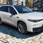 Driekwart vooraanzicht van 2025 Leapmotor C10 REEV in Pearl White kleur met 20-inch velgen, LED koplampen, zwart dak en moderne SUV-proporties geparkeerd op geplaveide straat met stedelijke gebouwen op de achtergrond.