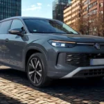 2025 Volkswagen Tayron SUV in grijsmetaalkleurige lak geparkeerd op kinderkopjes met moderne stadsgebouwen op de achtergrond, voor- en zijkant design tonend