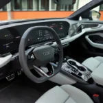 Interieurzicht van 2026 Audi A6 met gebogen digitaal dashboard met virtual cockpit display, MMI touchscreen, stuurwiel en lichtgekleurde stoelen met sfeerverlichting