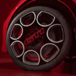 Detail aanzicht van 2026 Peugeot e-208 GTi wiel met 18-inch geperforeerd ontwerp met rood GTi logo in centrum, geïnspireerd door klassieke 205 GTi peperpot wielen