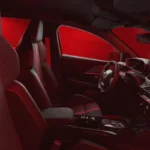Zijaanzicht van complete 2026 Peugeot e-208 GTi interieur met voor- en achterstoelen met rode accenten, sfeerverlichting, dashboard, en algemene cabine-indeling