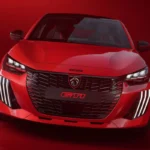 Volledig voorprofiel aanzicht van 2026 Peugeot e-208 GTi met complete voertuig houding, gemodificeerde wielkasten, prestatie wielen, en geïntegreerd voorspoiler ontwerp