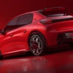 Volledig zijprofiel aanzicht van 2026 Peugeot e-208 GTi met complete voertuig proporties, verlaagde houding, uitlopende wielkasten, GTi wielen, en sportieve zijstyling