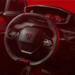 Interieur aanzicht van 2026 Peugeot e-208 GTi met dashboard, digitaal display met rode graphics, en GTi-gemerkt stuurwiel met rode accenten en geperforeerd leer