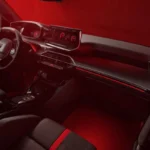 Groothoek aanzicht van 2026 Peugeot e-208 GTi voorinterieur met complete cockpit indeling, rode sfeerverlichting, stuurwiel, dashboard, en voorstoelen