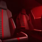 Achterbank aanzicht van 2026 Peugeot e-208 GTi interieur met achterstoelen met rode streep details, sfeerverlichting, en algemene achterpassagier ruimte