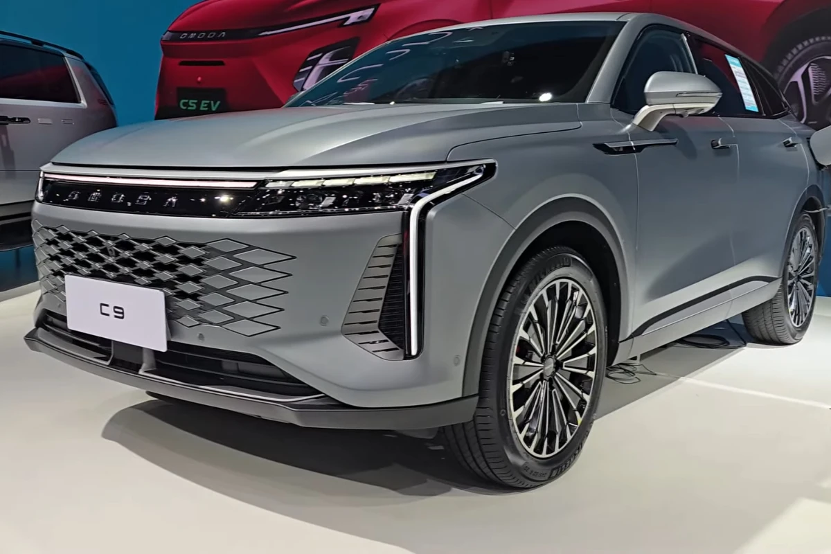 Voorkant driekwart zicht van zilveren Omoda 09 op autoshow met 134 LED dagrijverlichting, diamant-patroon grille, gedurfd voorbumper ontwerp en 20-inch lichtmetalen velgen met zichtbaar Omoda logo