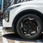 2026 Kia Sportage 18-inch zwarte lichtmetalen velg met vijfspaaks design, centrale Kia logo, Continental EcoContact 6 band en wit carrosserie paneel op stedelijke straat met zebrapad markeringen