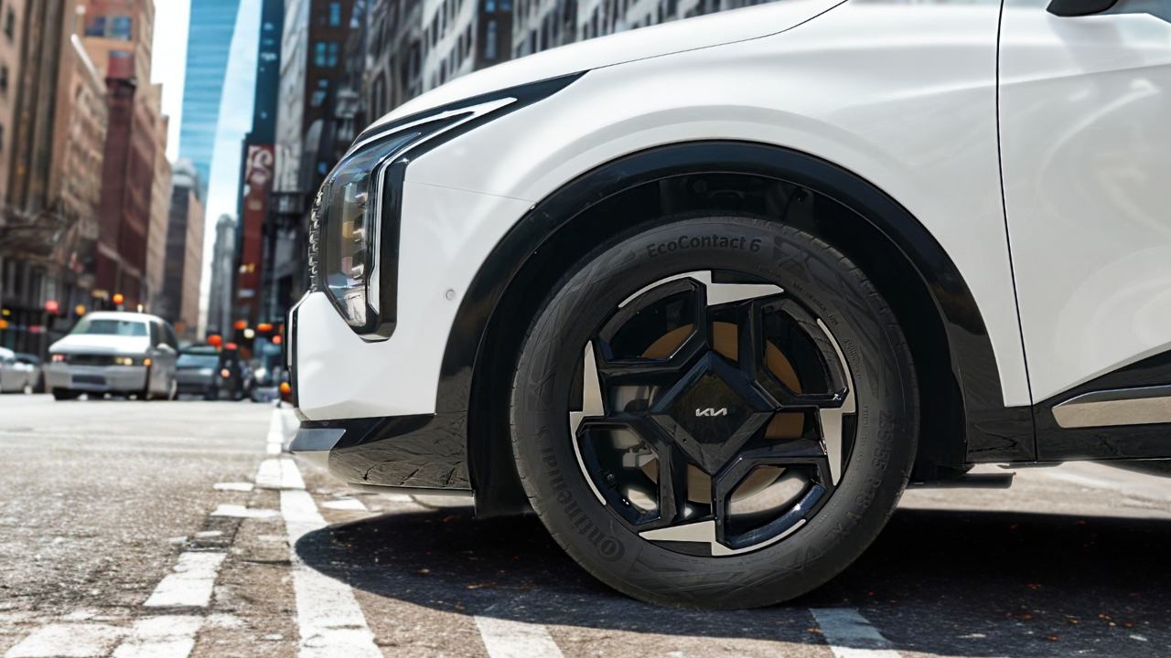2026 Kia Sportage 18-inch zwarte lichtmetalen velg met vijfspaaks design, centrale Kia logo, Continental EcoContact 6 band en wit carrosserie paneel op stedelijke straat met zebrapad markeringen