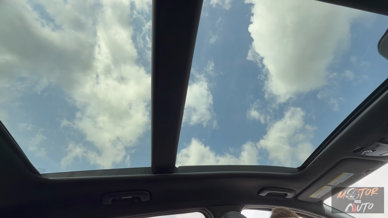 2026 Kia Sportage panoramadak met blauwe lucht en wolken door grote glas opening met zonnescherm en dak bediening zichtbaar
