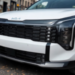 2026 Kia Sportage close-up met grote zwarte honingraat grille patroon, zilver Kia logo, LED koplamp behuizing, witte voorbumper en parkeersensoren op stedelijke straat