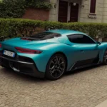 Achter driekwart aanzicht van turquoise 2026 Maserati MCPura op kinderkopjes binnenplaats met slanke achterlichten, herzien achterbumperontwerp, en laag-liggende supercar verhoudingen