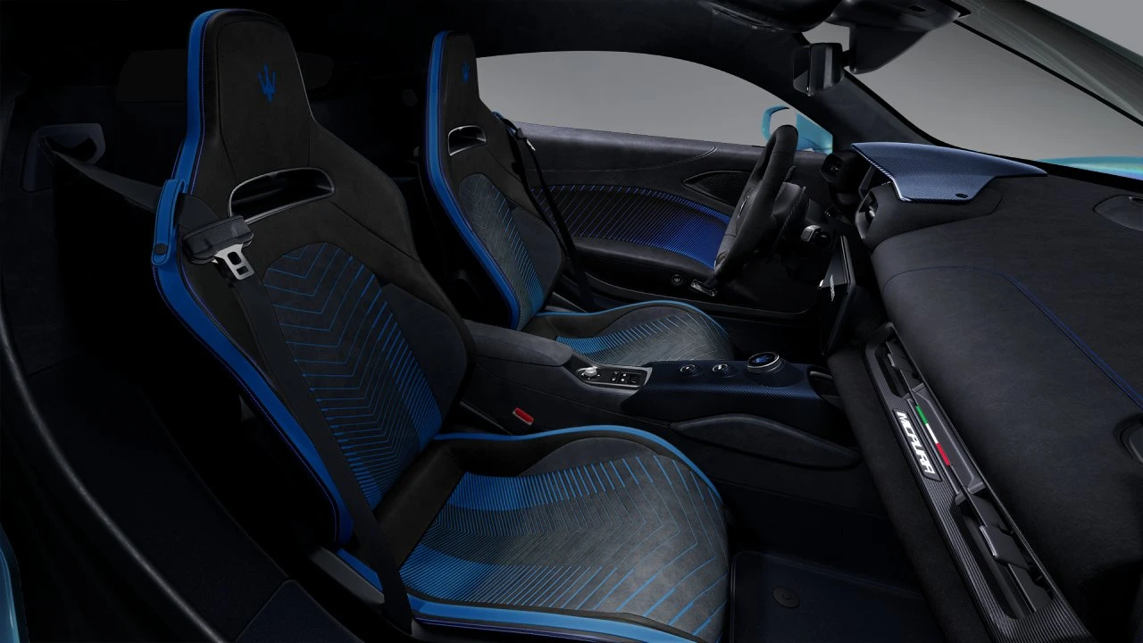 Volledige interieur cabine aanzicht van 2026 Maserati MCPura met racing kuipstoelen met blauwe laser-geëtste patronen, centrale console met transmissie bedieningselementen, carbon fiber accenten, en uitgebreide bestuurder-gerichte cockpit layout