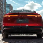 2026 Mazda 6e achteraanzicht in Soul Red Crystal met volledige-breedte LED achterlichten, MAZDA letters, en liftback ontwerp in stedelijke omgeving