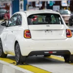 Achter drie-kwart aanzicht van witte Fiat 500 Hybrid met kenmerkende LED achterlichten en FIAT badge in moderne fabriek omgeving