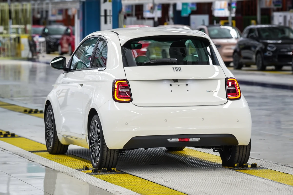 Achter drie-kwart aanzicht van witte Fiat 500 Hybrid met kenmerkende LED achterlichten en FIAT badge in moderne fabriek omgeving