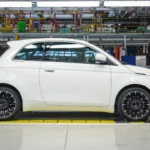 Complete side view of white Fiat 500 Hybrid on factory production line showing classic Italian design proportions and modern wheel design
