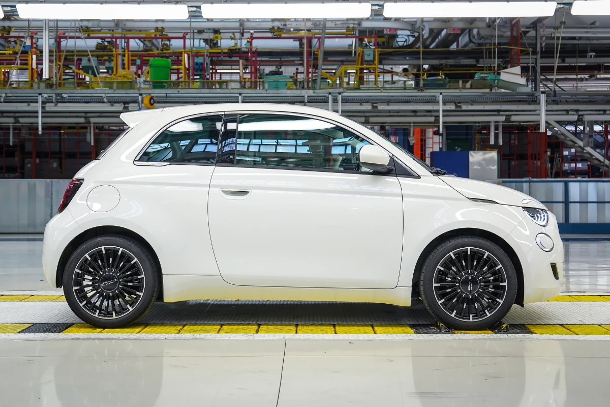 Complete side view of white Fiat 500 Hybrid on factory production line showing classic Italian design proportions and modern wheel design