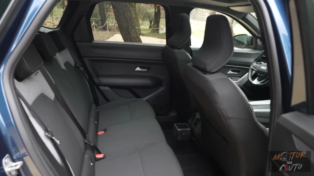 Achterpassagiersruimte van de 2025 Dacia Bigster met donkere beklede stoelen, deurpanelen en raamzicht met bomen zichtbaar buiten