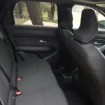 Achterpassagiersruimte van de 2025 Dacia Bigster met donkere beklede stoelen, deurpanelen en raamzicht met bomen zichtbaar buiten