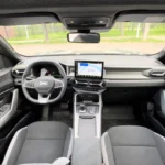 Volledig dashboardzicht van 2025 Dacia Bigster interieur met digitaal instrumentenpaneel, centrale touchscreen, stuurwiel met DC-logo en tweekleurig interieurontwerp met automatische versnelling