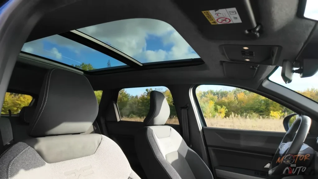Interieurcabine van 2025 Dacia Bigster met groot panoramadak, tweekleurige stoelen met DC-branding, stuurwiel en dashboard met blauwe lucht zichtbaar door glazen dak