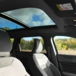 Interieurcabine van 2025 Dacia Bigster met groot panoramadak, tweekleurige stoelen met DC-branding, stuurwiel en dashboard met blauwe lucht zichtbaar door glazen dak