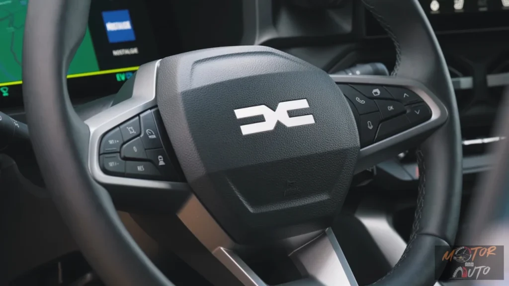 Stuurwiel van 2025 Dacia Bigster met zwarte afwerking en prominent DC-logo in het midden, bedieningsknoppen op spaken en gedeeltelijk zicht op digitaal instrumentenpaneel