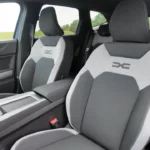 Close-up van 2025 Dacia Bigster voorstoelen met tweekleurige grijs-witte bekleding met geëmbosseerde DC-logo's op rugleuningen en premium stikdetails