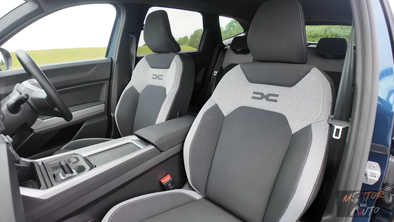 Close-up van 2025 Dacia Bigster voorstoelen met tweekleurige grijs-witte bekleding met geëmbosseerde DC-logo's op rugleuningen en premium stikdetails