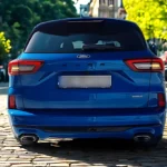 2025 Ford Kuga recht achteraanzicht met gemoderniseerd LED achterlichtontwerp, prominente Ford letters, dubbele uitlaatpijpen en verfijnde achterbumperontwerp in stadsomgeving