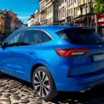 2025 Ford Kuga vanuit driekwart achterperspectief op Europese kinderkopjesstraat, bijgewerkte achterlichtontwerp, dubbele uitlaatpijpen en slanke SUV-silhouet in stedelijke omgeving tonend