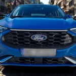 Gedetailleerde close-up van 2025 Ford Kuga voorkant grille met kenmerkend zeshoekig mesh patroon, chromen accenten en centraal gepositioneerd Ford ovaal badge met premium afwerking