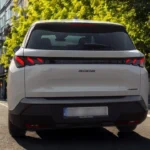 Achteraanzicht van witte 2025 Peugeot 5008 met kenmerkende triple LED achterlichten en PEUGEOT letters op stadsstraat met gebouwen